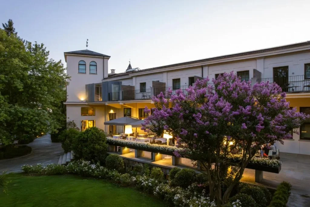 Kameralny ogród z kwitnącymi drzewami i oświetlonym tarasem przy eleganckim budynku – Alter Hotel, Lublin.