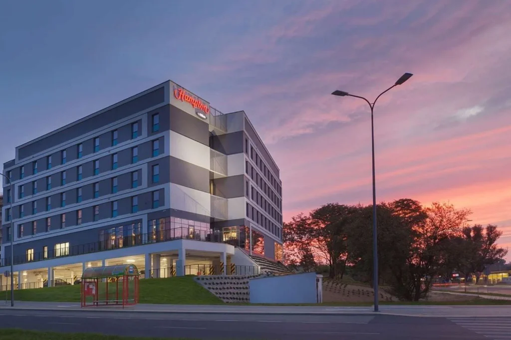 Nowoczesny budynek hotelowy z przeszklonym parterem na tle kolorowego zachodu słońca w Hampton by Hilton Lublin, Lublin, Poland