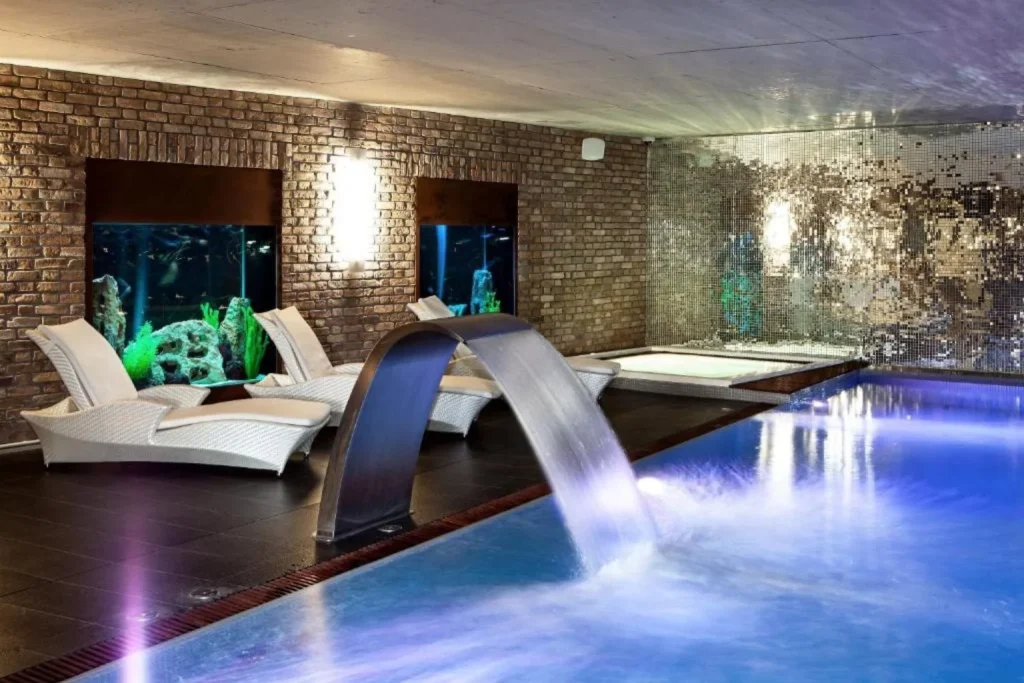 Indoor spa pool with hydrotherapy waterfall, relaxation loungers, and aquarium displays at Hotel Alter in Lublin, Poland.