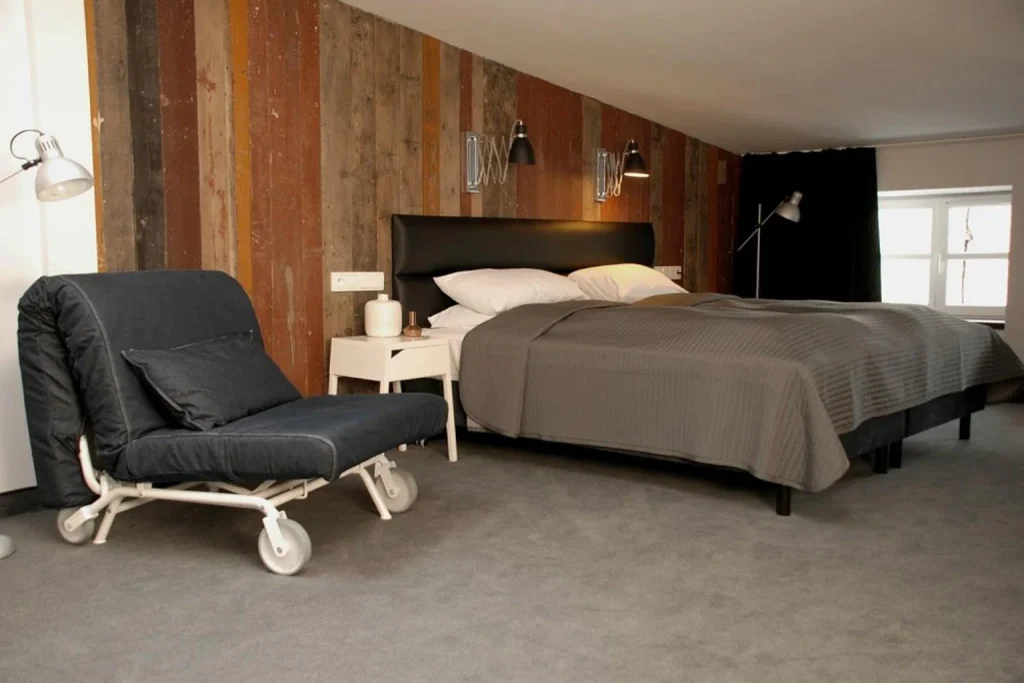 Stylowy pokój z dużym łóżkiem, fotelem i dekoracyjną drewnianą ścianą w Hotel Grodzka 20 Lublin