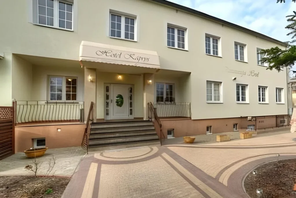 Front entrance of Hotel Kaprys in Lublin, Poland, featuring a cream-colored facade, landscaped walkway, and welcoming main entrance.