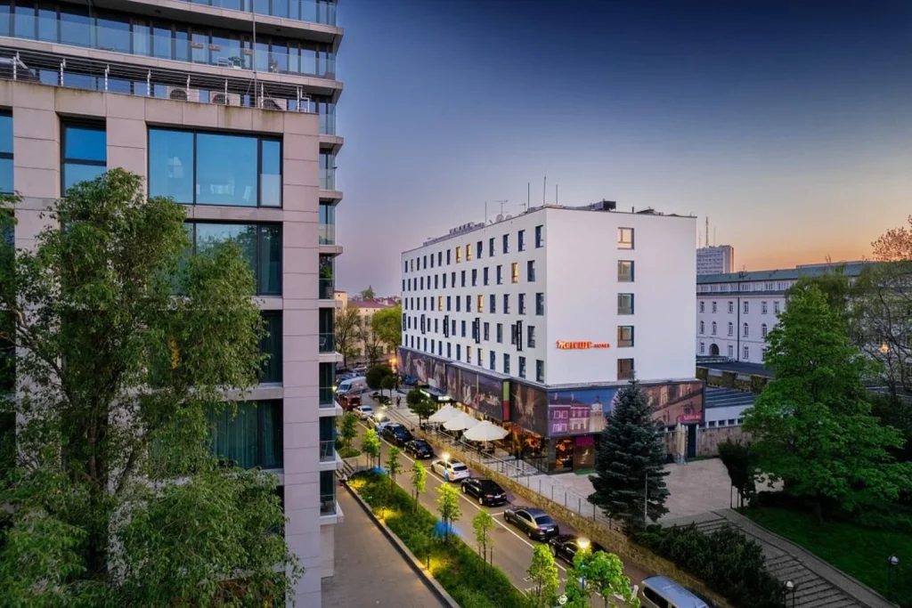White exterior with large windows, outdoor seating, and a convenient location surrounded by city streets and green spaces at Hotel Mercure Lublin Centrum