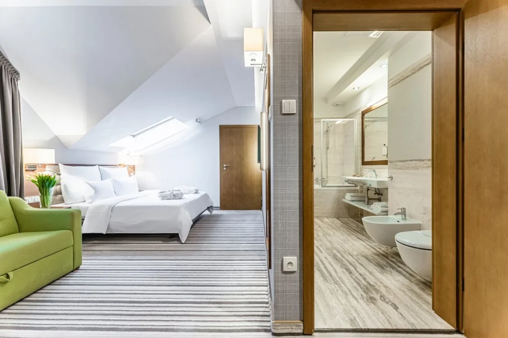 Jasny pokój na poddaszu z dużym łóżkiem, zieloną sofą oraz przestronną łazienką w Hotel Wieniawski Lublin.