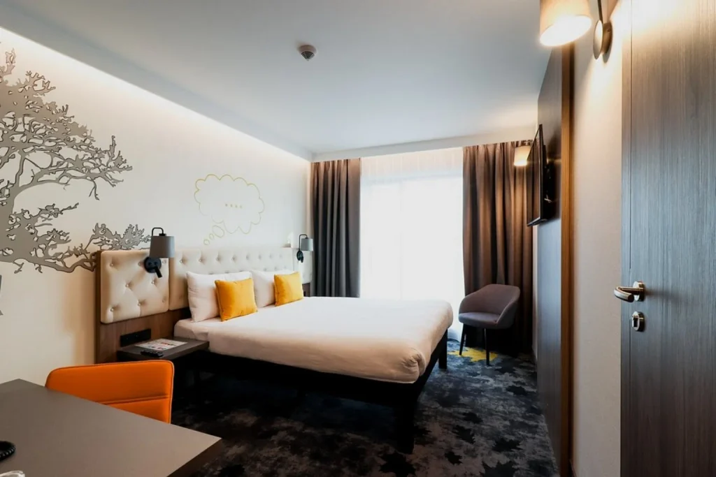 Nowoczesny pokój z dużym łóżkiem, dekoracyjną ścianą i kolorowymi akcentami w ibis Styles Lublin Stare Miasto
